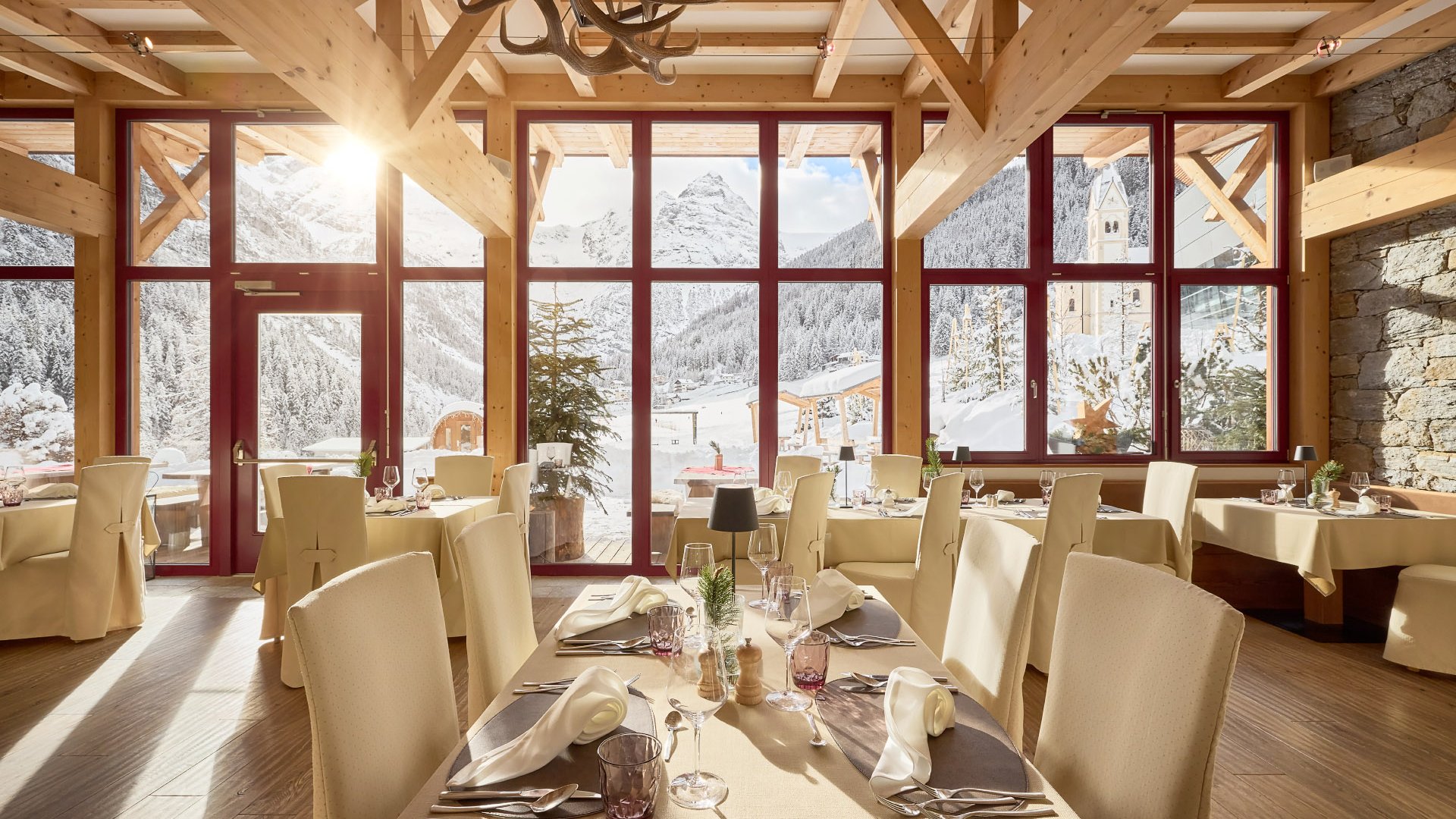 Eleganter Restaurantbereich im Hotel Bella Vista in Südtirol mit großen Fenstern, die einen sonnendurchfluteten Raum und Aussicht auf die verschneite Alpenlandschaft bieten.