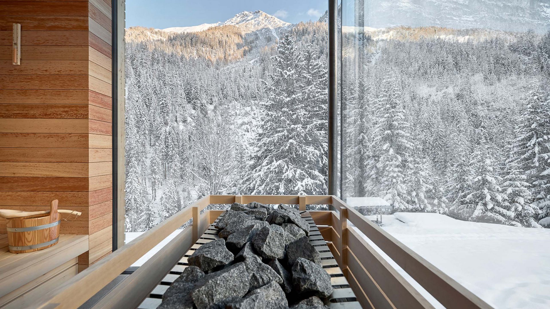 Gemütliche Sauna mit großer Glasfront im Hotel Bella Vista, die den Blick auf die schneebedeckte Waldlandschaft freigibt und eine Atmosphäre der Ruhe schafft.