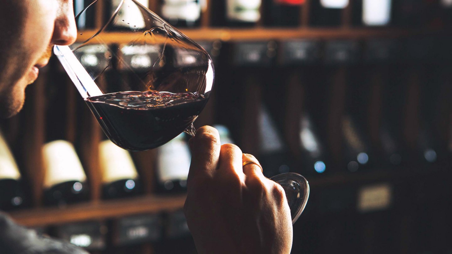 Ein Moment der Weinverkostung im Hotel Bella Vista, bei dem ein Gast die Qualität eines edlen Rotweins vor einem Weinkeller-Hintergrund prüft.